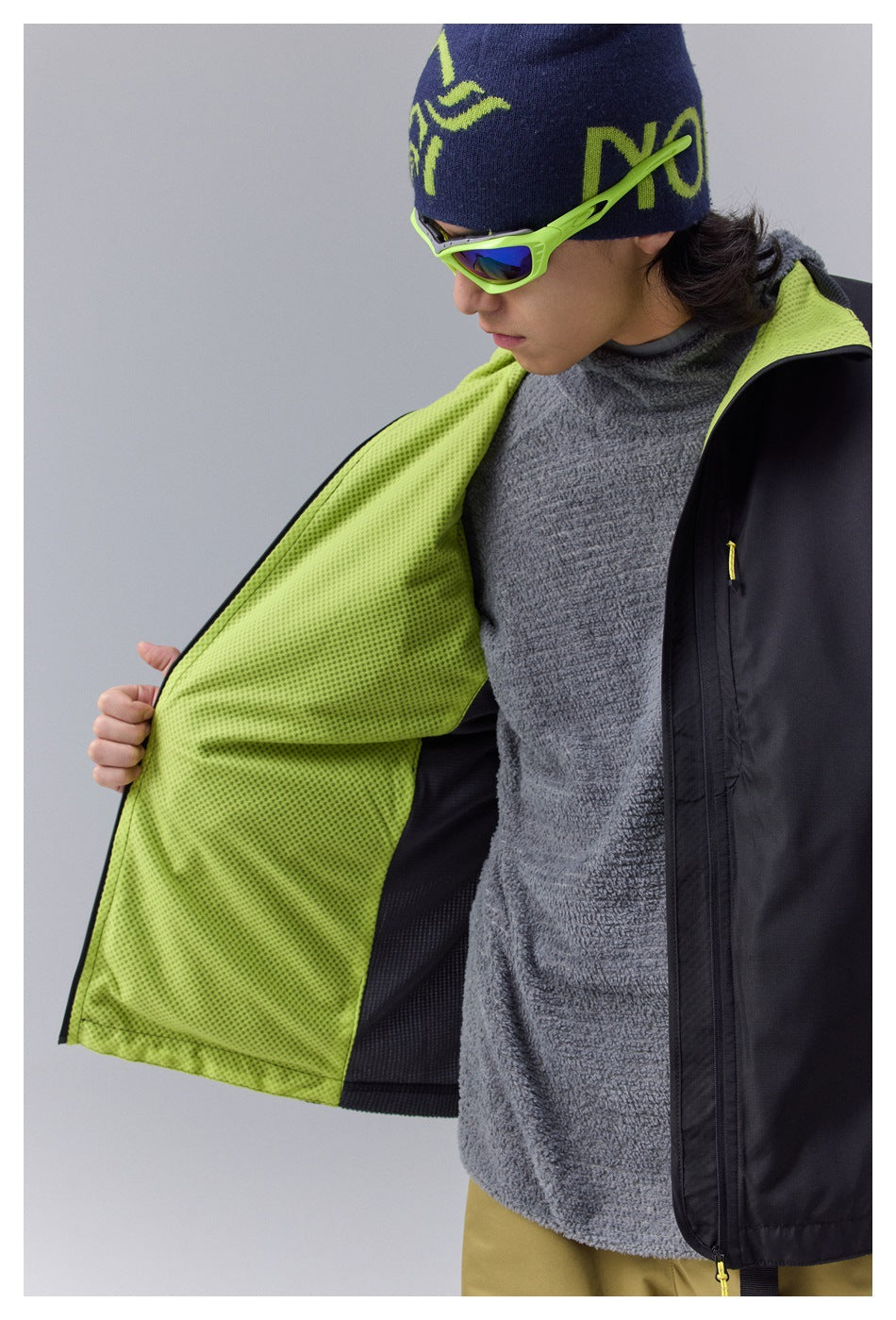 Close view of a black jacket opened to reveal bright lime perforated lining and a gray fleece layer.