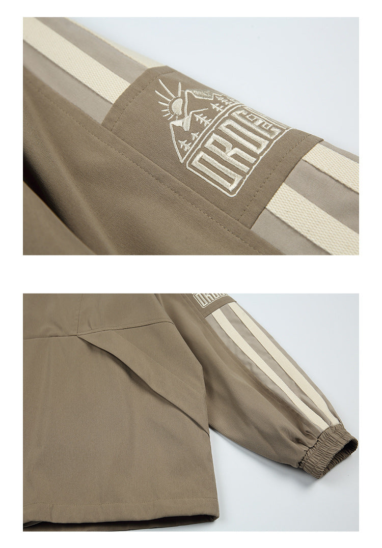 Close-up of a taupe jacket sleeve with cream stripes and a white embroidered mountain-and-sun graphic.