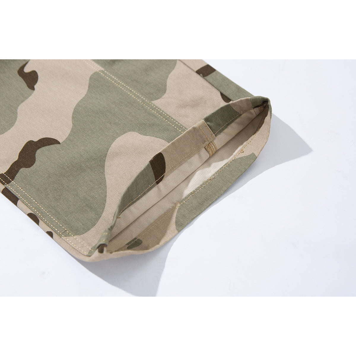 Close-up of a folded leg opening on beige, olive, and brown camouflage pants, showing the hem stitching.