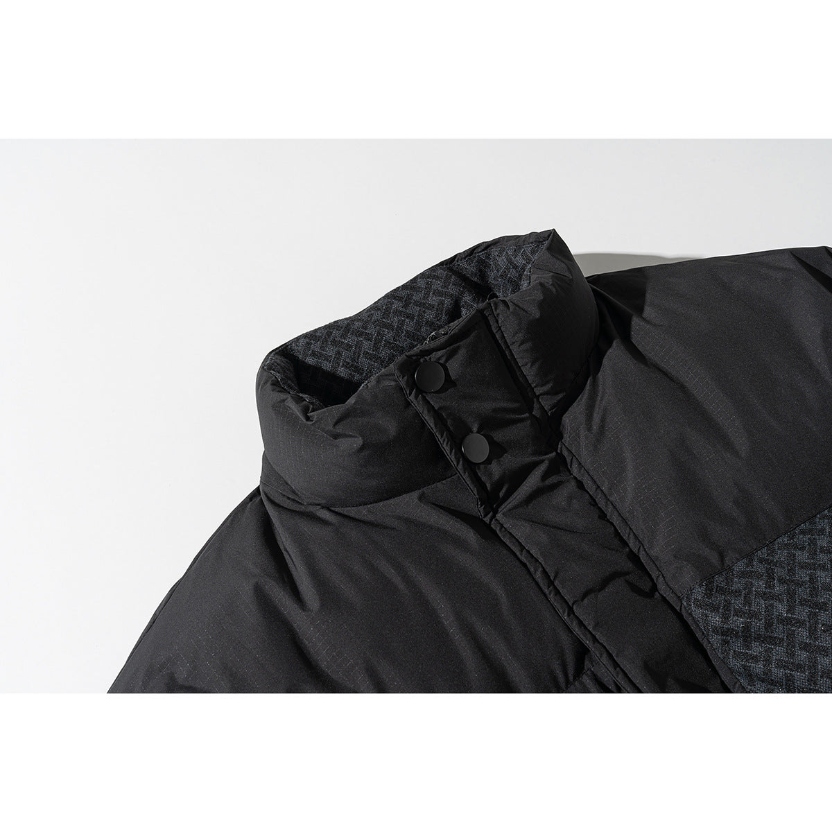 Close-up of a black jacket collar with patterned lining and two black snap buttons.