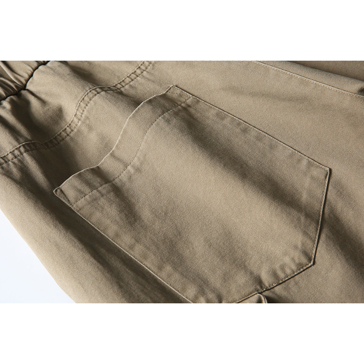 Close-up of a stitched patch pocket on taupe trousers.