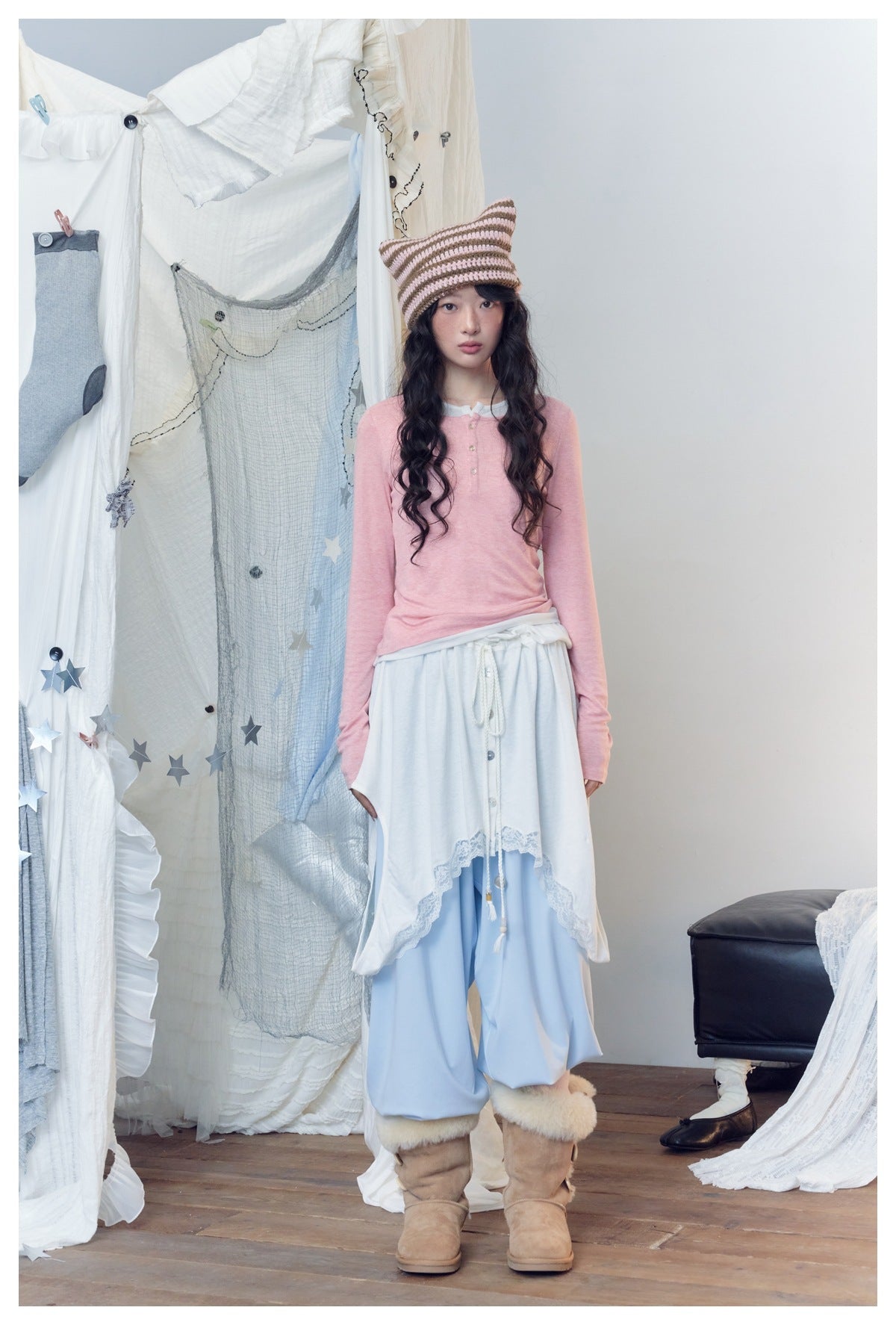 Model wearing pink henley top with white trim, styled with a striped knit hat, white skirt, light blue pants and boots