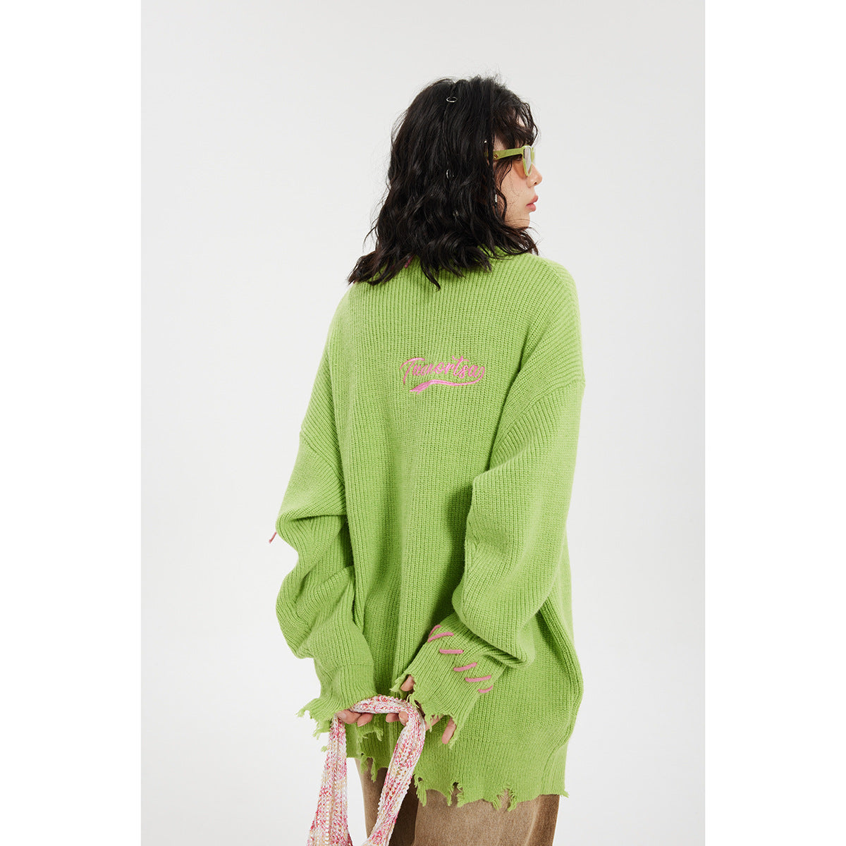 Rear view of a model wearing a lime-green sweater with pink script embroidery, pink accents, and a distressed hem.