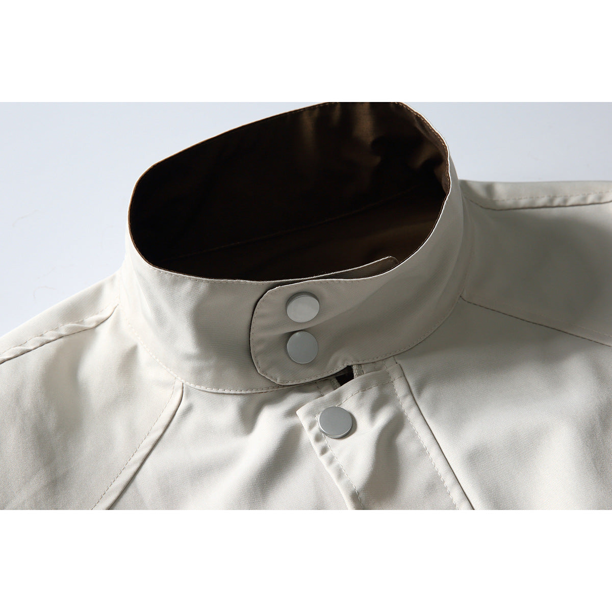 Close-up of an ivory jacket's stand collar, dark lining, and silver snap buttons.