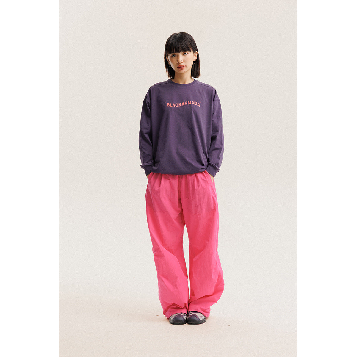 Model wearing a purple long-sleeve shirt with coral chest lettering and loose bright pink pants.