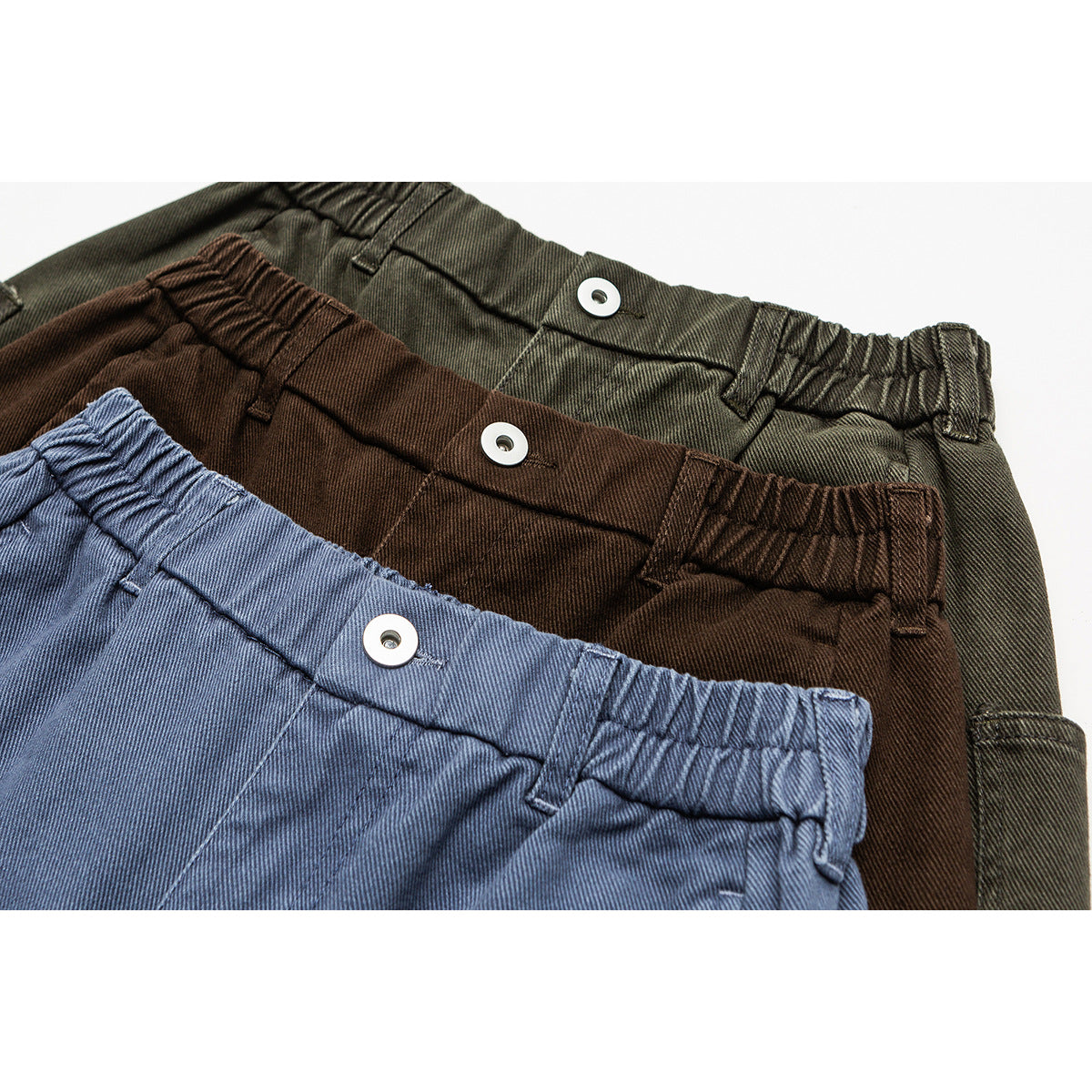 Close-up of elastic-waist trousers in blue, brown, and olive, showing metal buttons and belt loops.