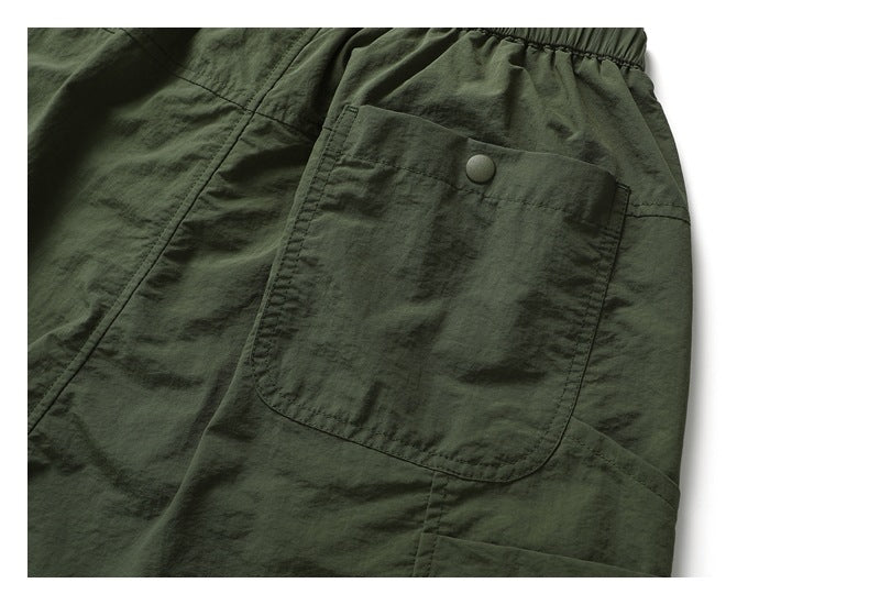 Close-up of dark olive shorts with a large patch pocket and snap button beside the elastic waistband.