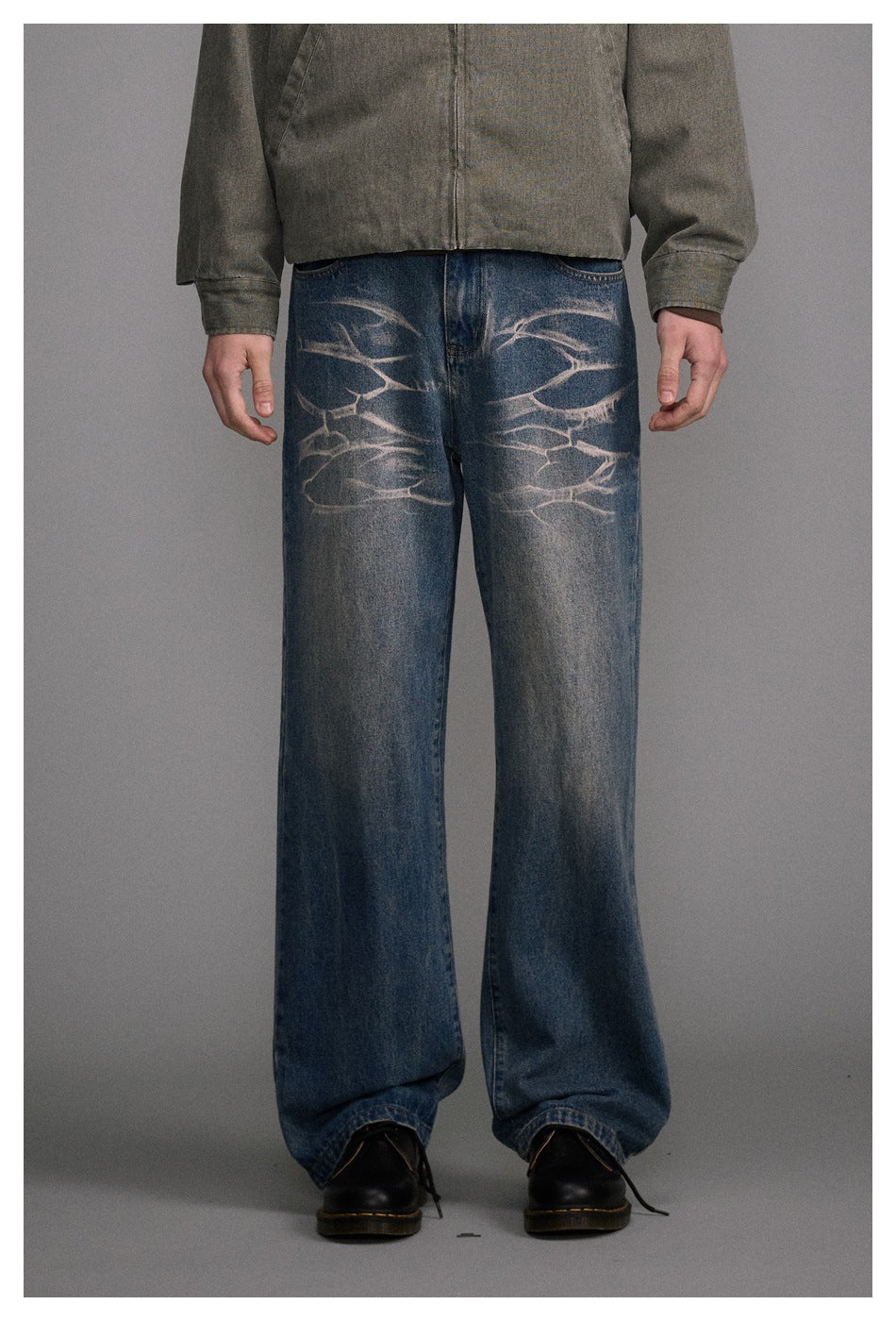 Close front view of a model wearing loose blue jeans with pale abstract fading across the thighs.