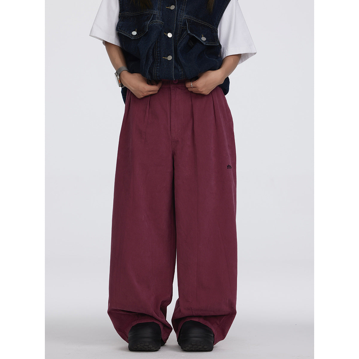 Model wearing oversized burgundy wide-leg pants with a dark denim vest and white T-shirt, front view.
