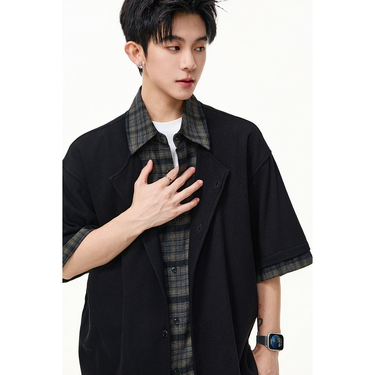 Close view of a model wearing a black short-sleeve overshirt layered over a dark plaid button-up shirt.