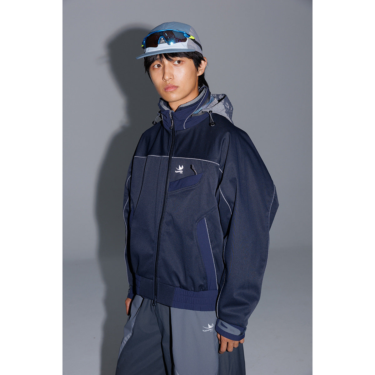 Model wearing a navy hooded zip jacket with gray trim and dark gray pants.
