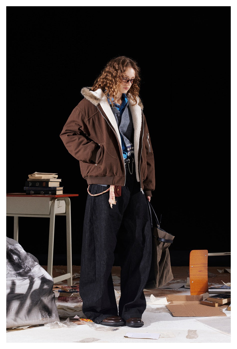 Full-length angled view of a model wearing an open brown fur-trimmed hooded jacket and wide dark trousers.