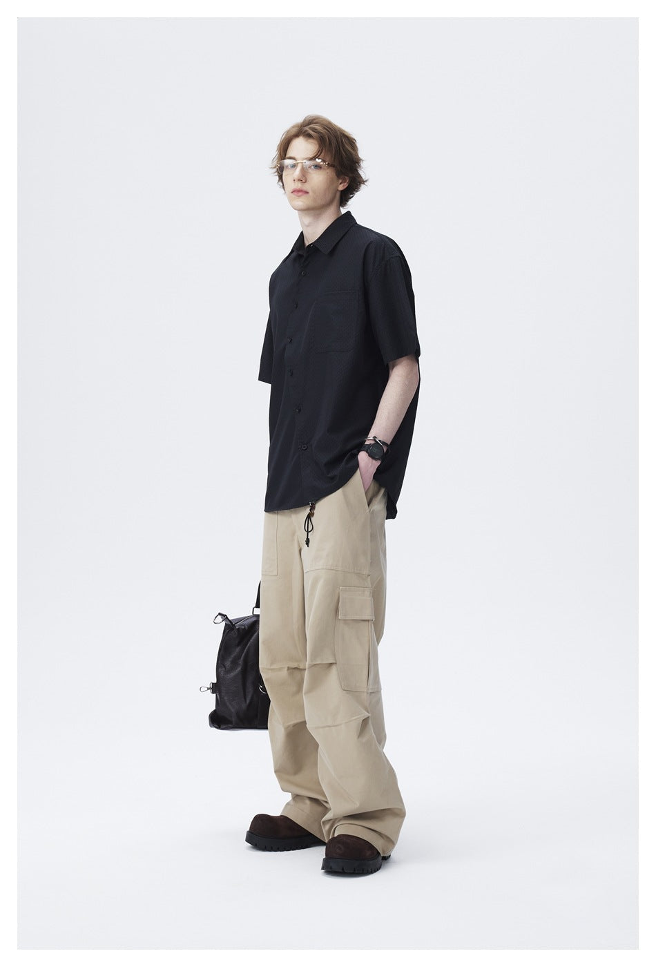 Model in a black short-sleeve shirt with a chest pocket and relaxed fit, angled view with khaki cargo pants