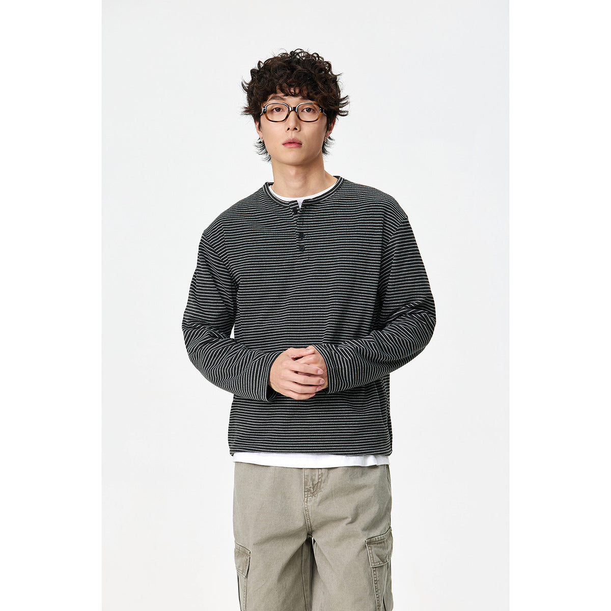 Model wearing a black thin-striped long-sleeve henley over a white shirt with khaki cargo pants.