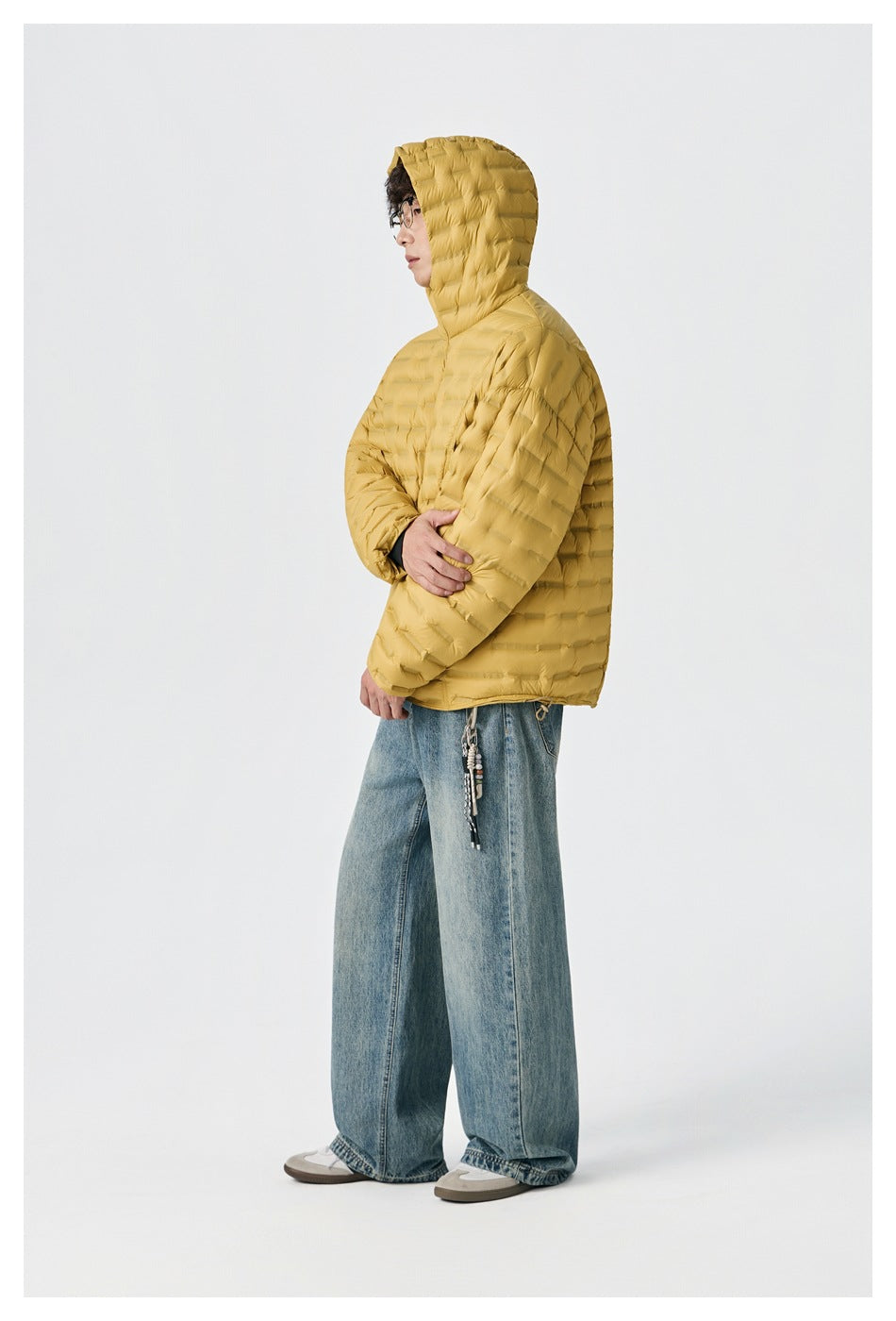 Side view of a model wearing a mustard-yellow hooded quilted jacket and loose light-wash jeans.