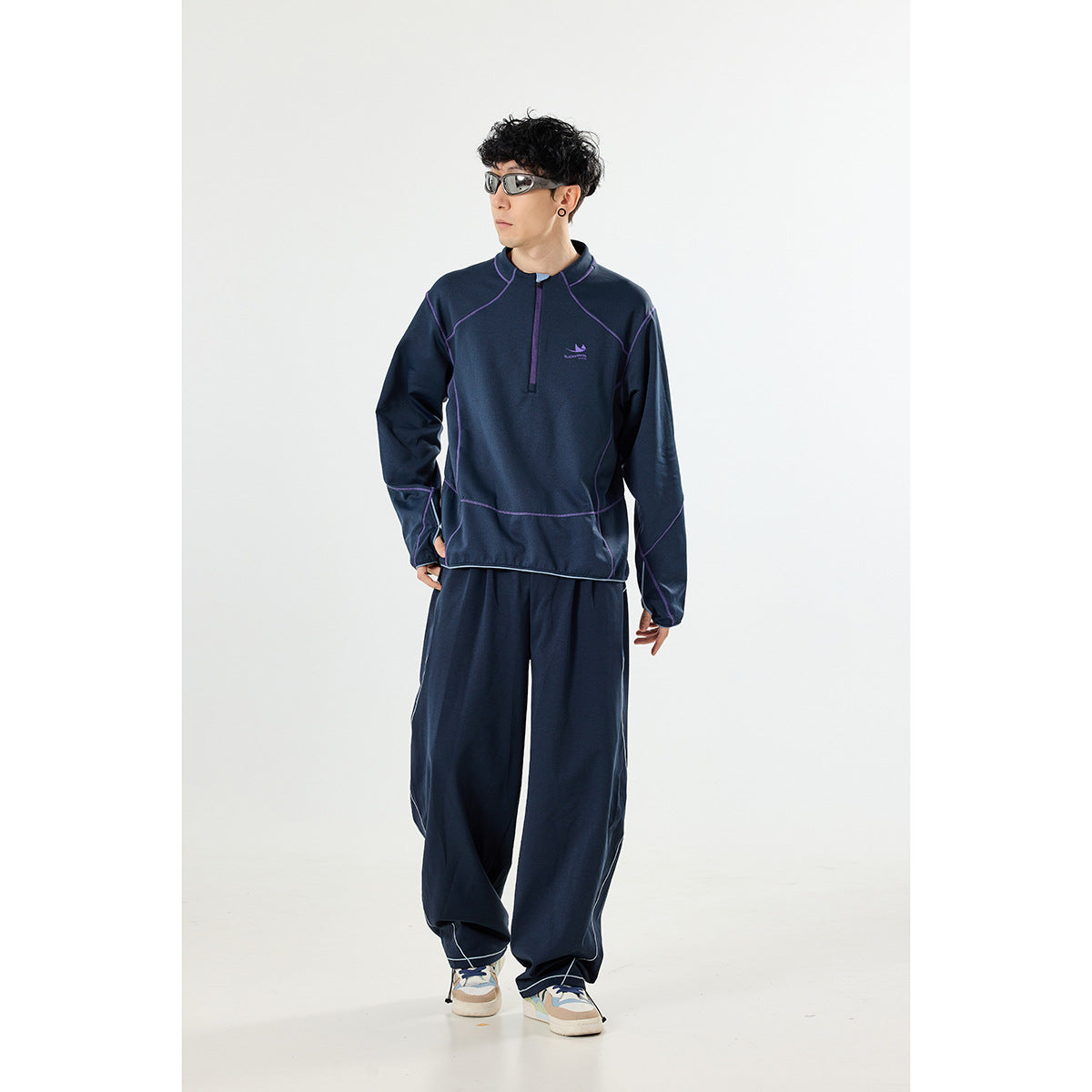 Man wearing a navy quarter-zip pullover with purple seam piping and loose matching pants.