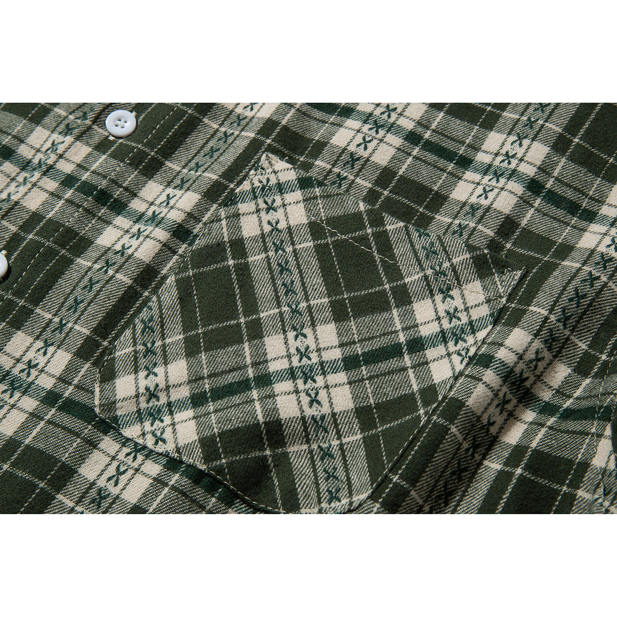 Close-up of a stitched chest pocket on a dark green and cream plaid shirt.