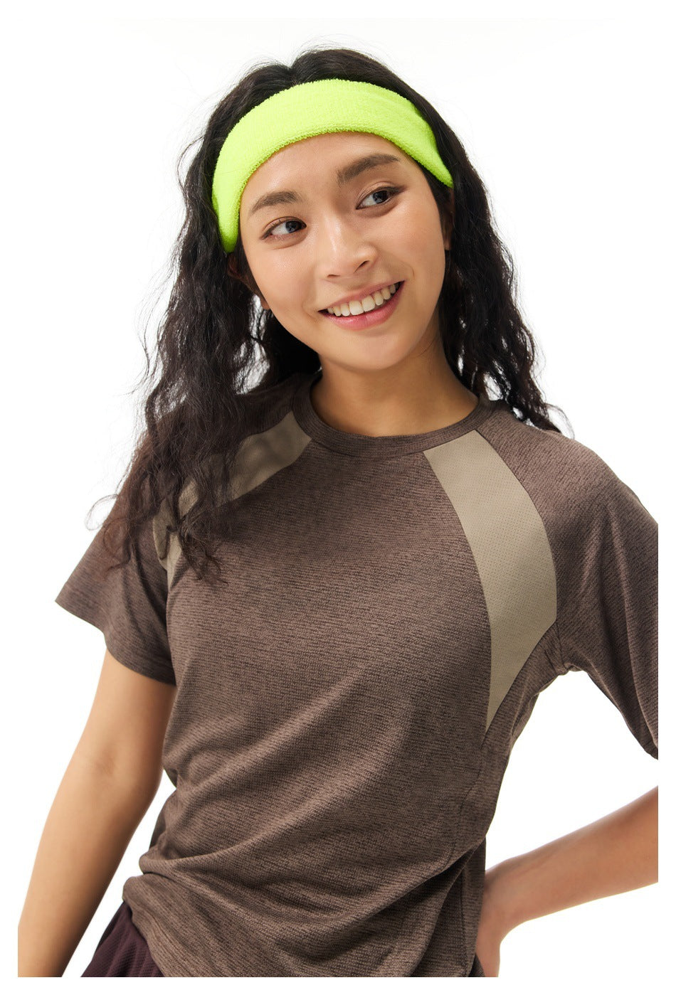 Close view of a model wearing a brown athletic top with taupe shoulder panels and a neon yellow-green headband.