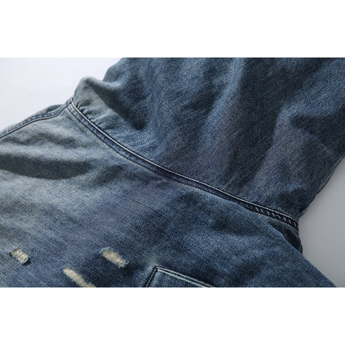 Close-up of the back of a blue denim jacket, showing a diagonal seam, faded areas and distressed tears.