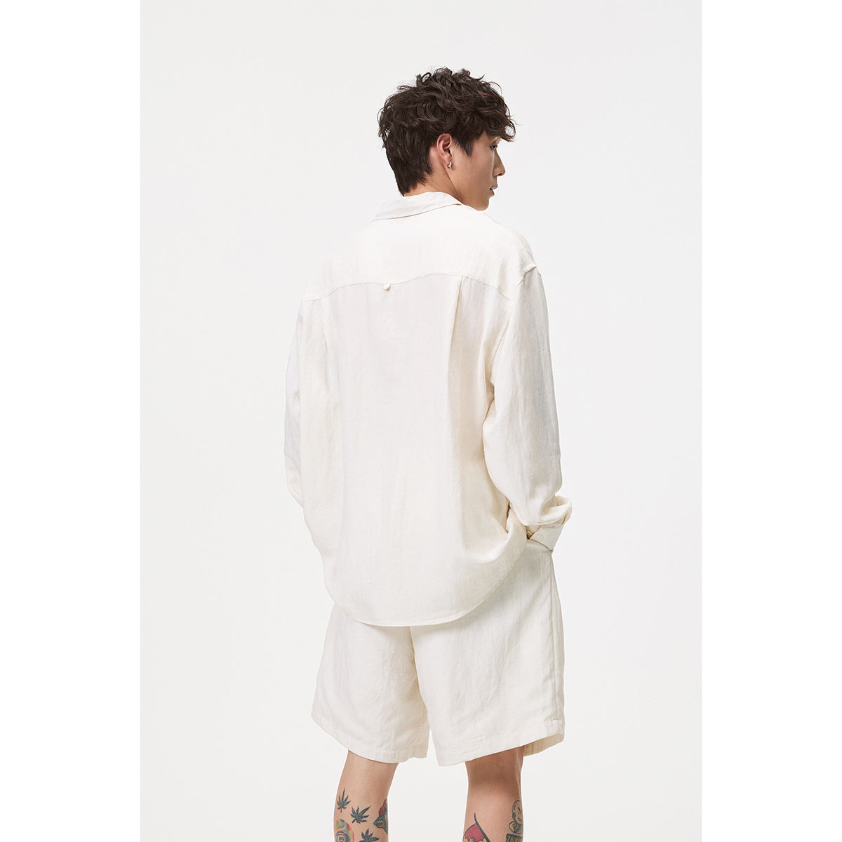 Back view of a man wearing an off-white long-sleeve shirt and matching shorts.