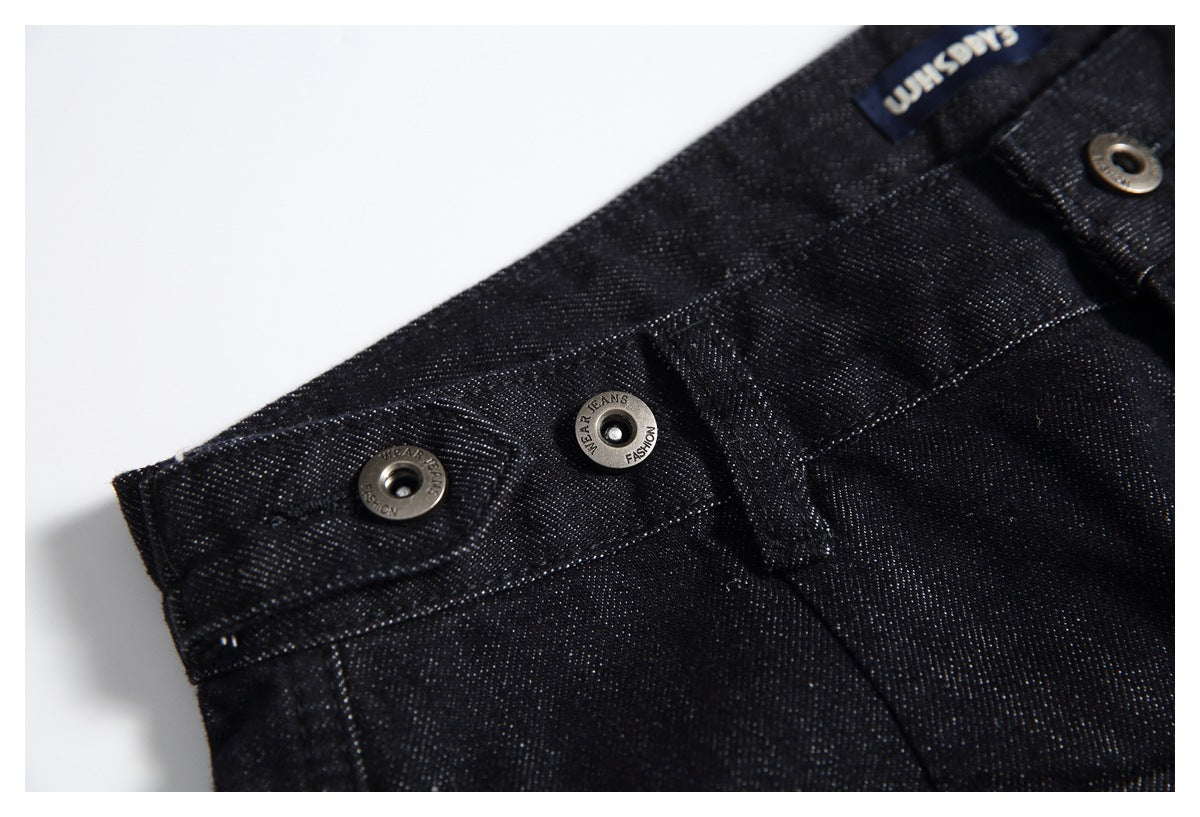 Close-up of black jeans showing the waistband, metal buttons, stitching and a blue label.
