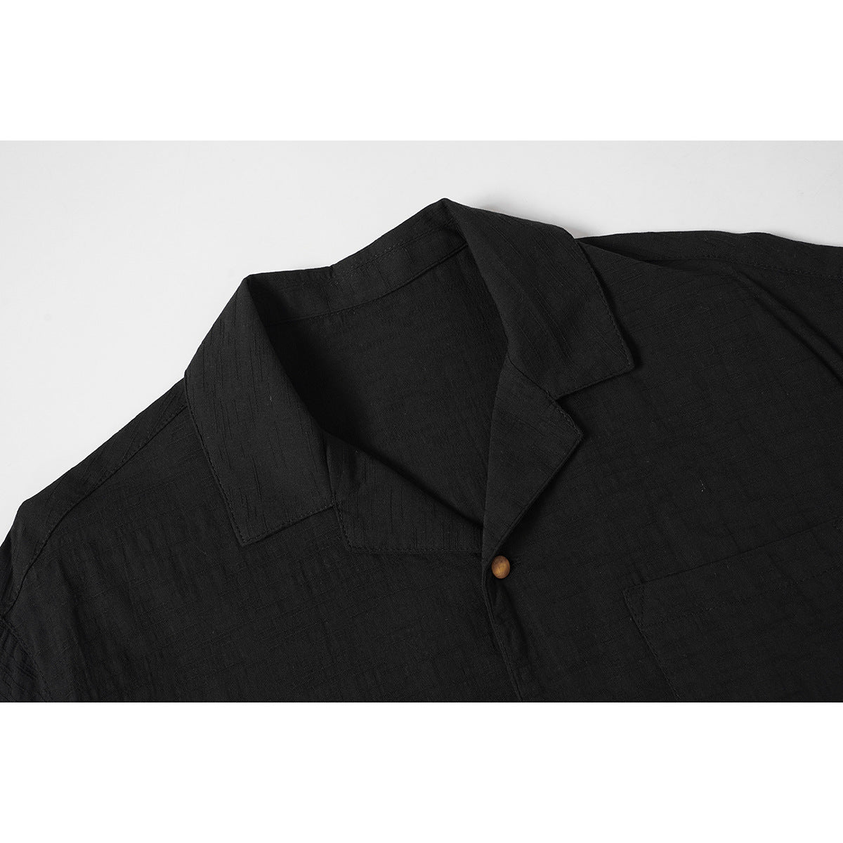 Close-up of a black short-sleeve shirt showing its notched collar and a wood-tone button.
