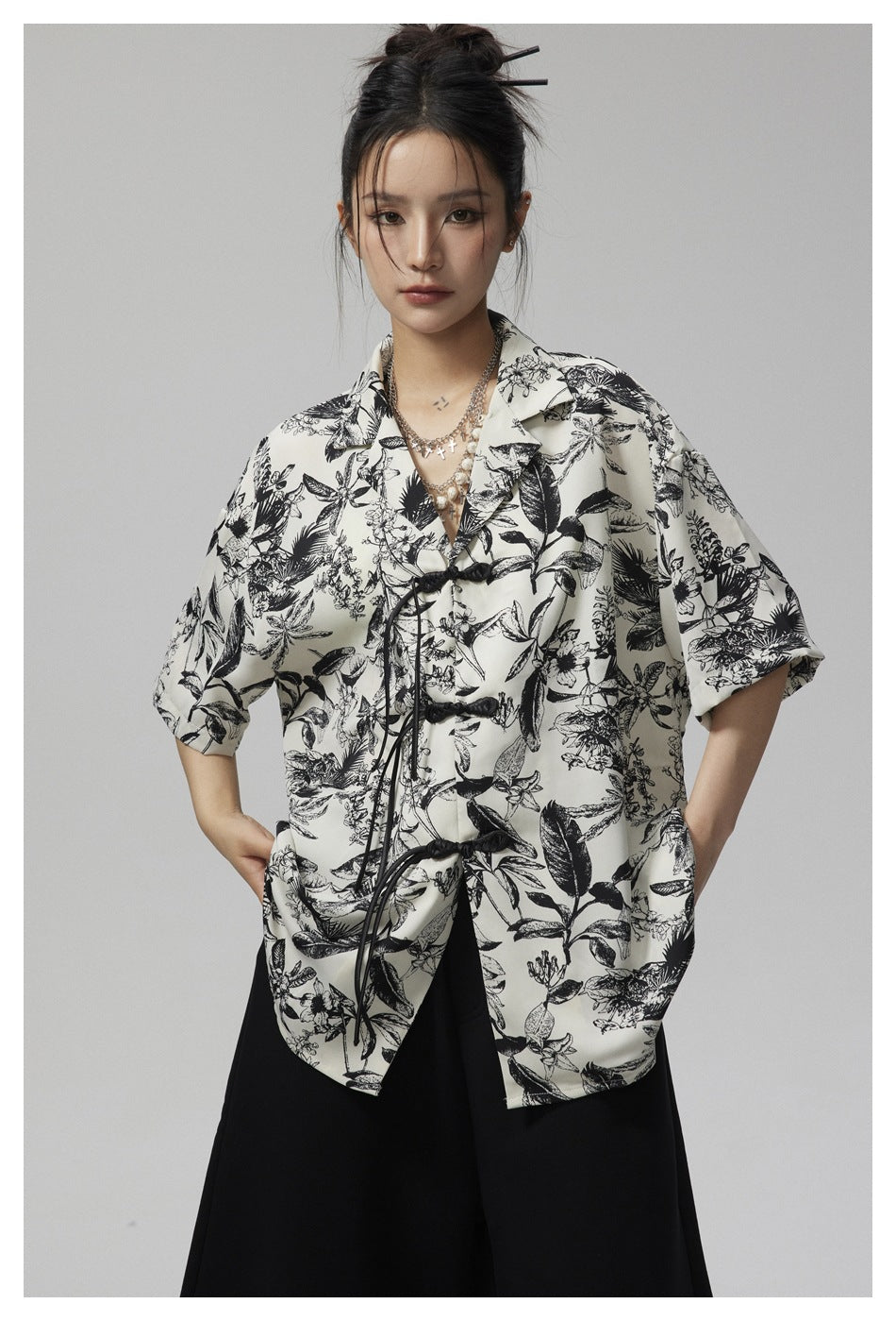Closer view of a model in an ivory shirt with black botanical print, wide sleeves and black frog closures.