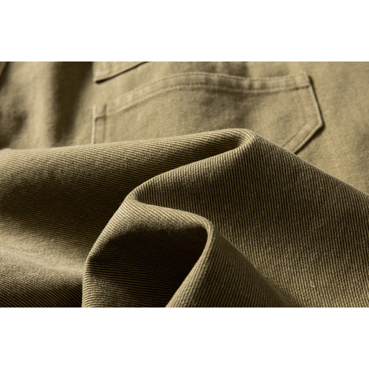 Macro view of olive-khaki shorts fabric folded beside a stitched patch pocket.