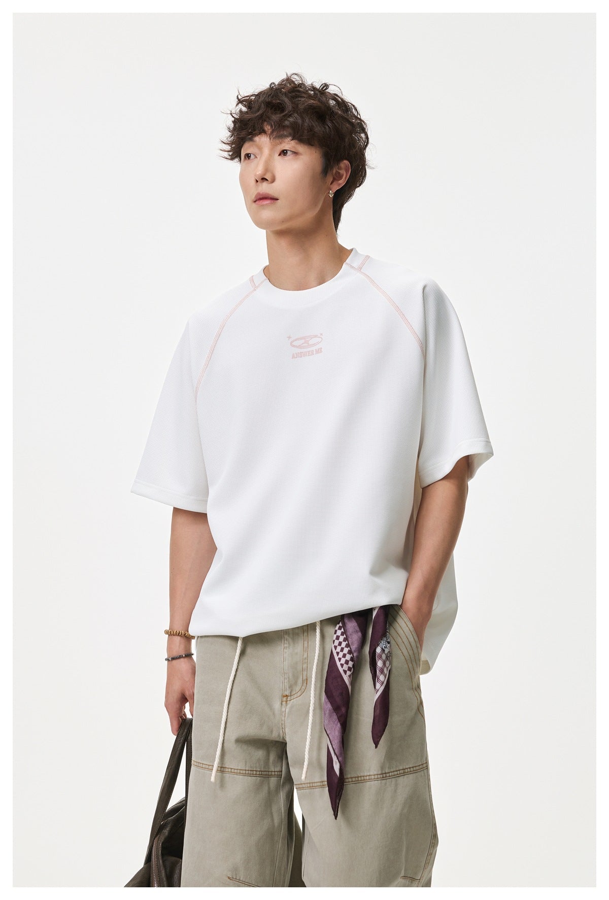 Man in a white waffle-textured raglan T-shirt with pink stitching and chest logo, three-quarter view with khaki pants