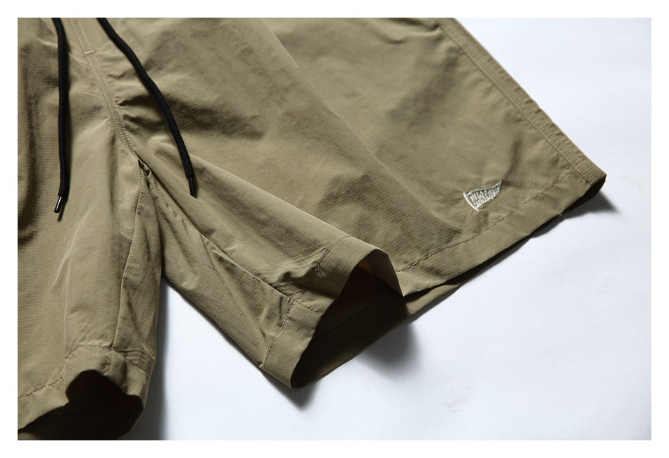 Close-up of the olive-khaki shorts' hem, black drawstrings and small embroidered emblem.