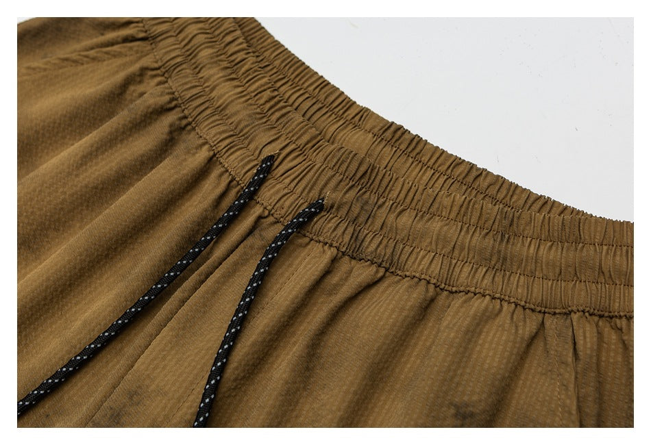 Close-up of brown shorts with a gathered elastic waistband and black drawcords with white flecks.