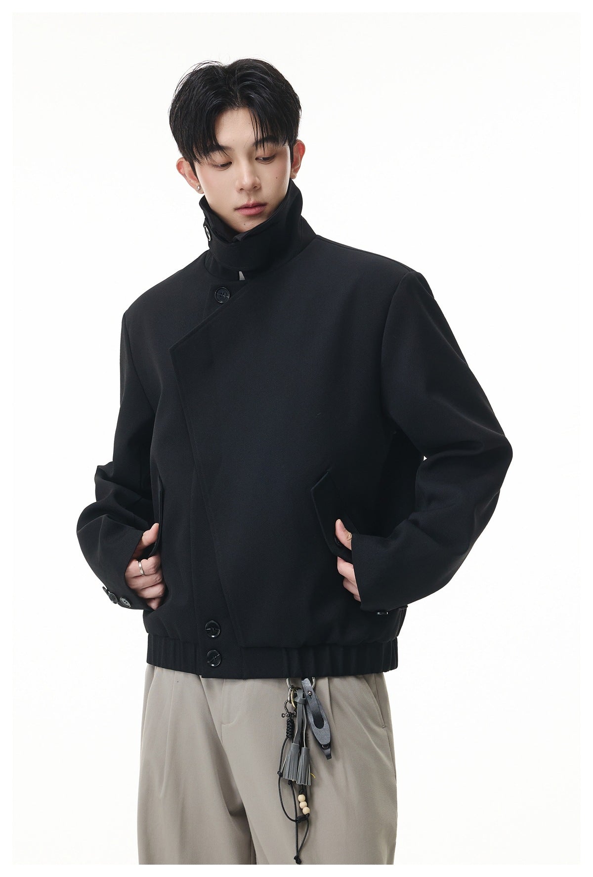 Model wearing a black jacket with a high collar, asymmetrical button front, and angled pockets.