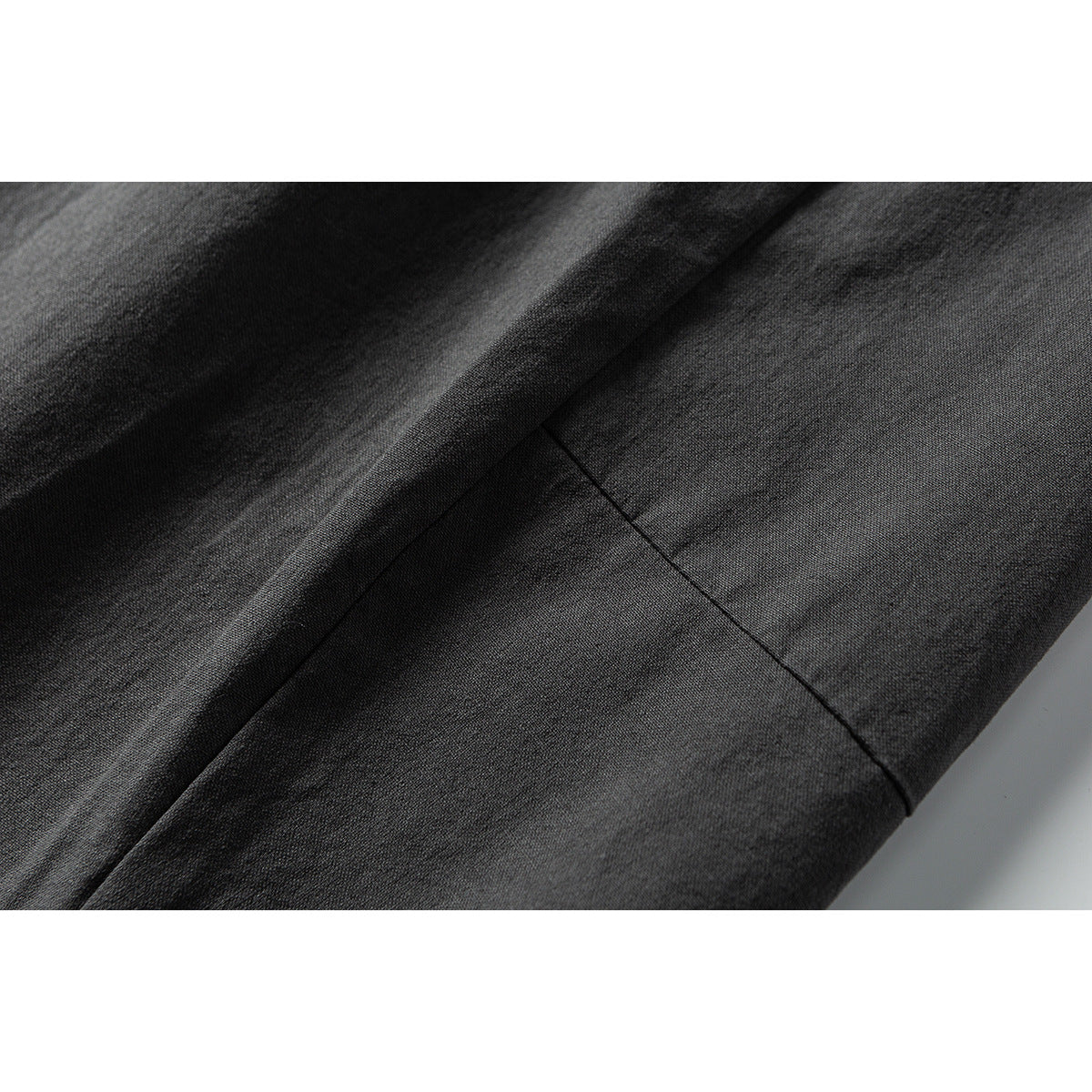 Close-up of charcoal fabric with a diagonal fold and stitched seam.