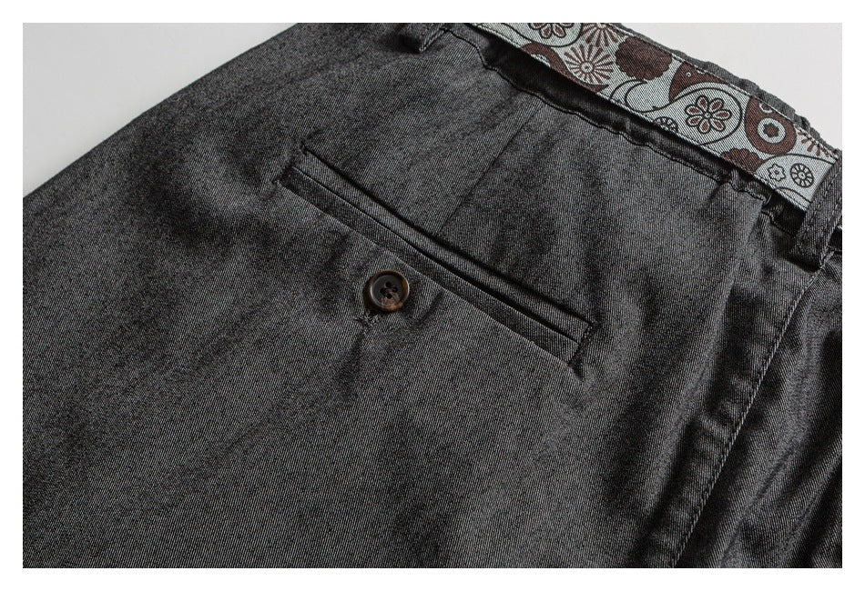 Close-up of charcoal trousers showing a buttoned rear welt pocket and patterned inner waistband.