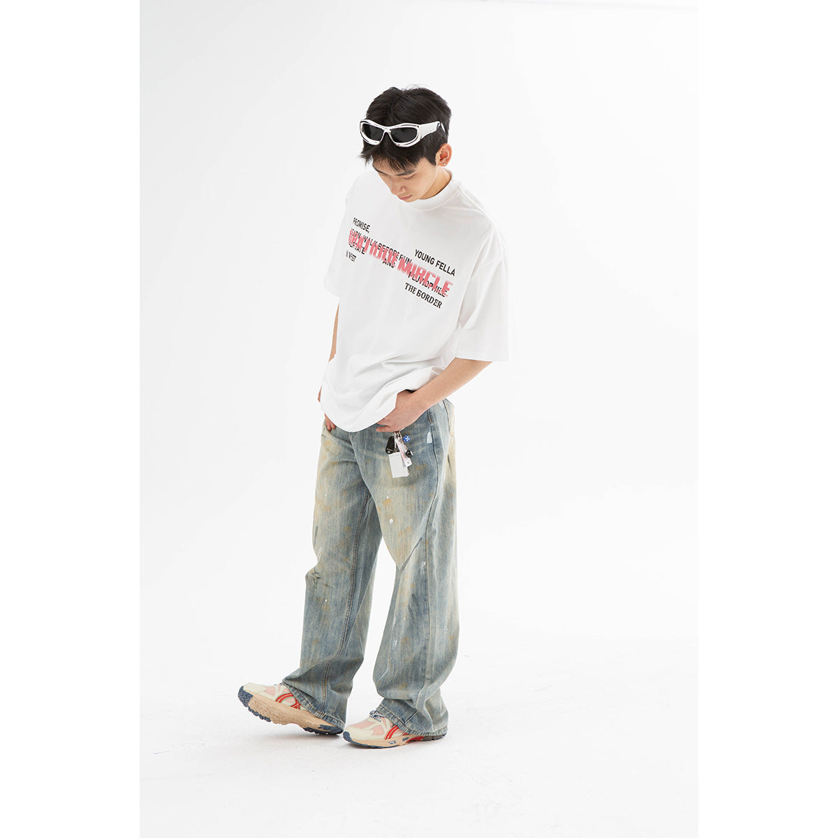 Full-length model wearing a white graphic T-shirt and extremely wide, faded blue jeans with paint-like marks.