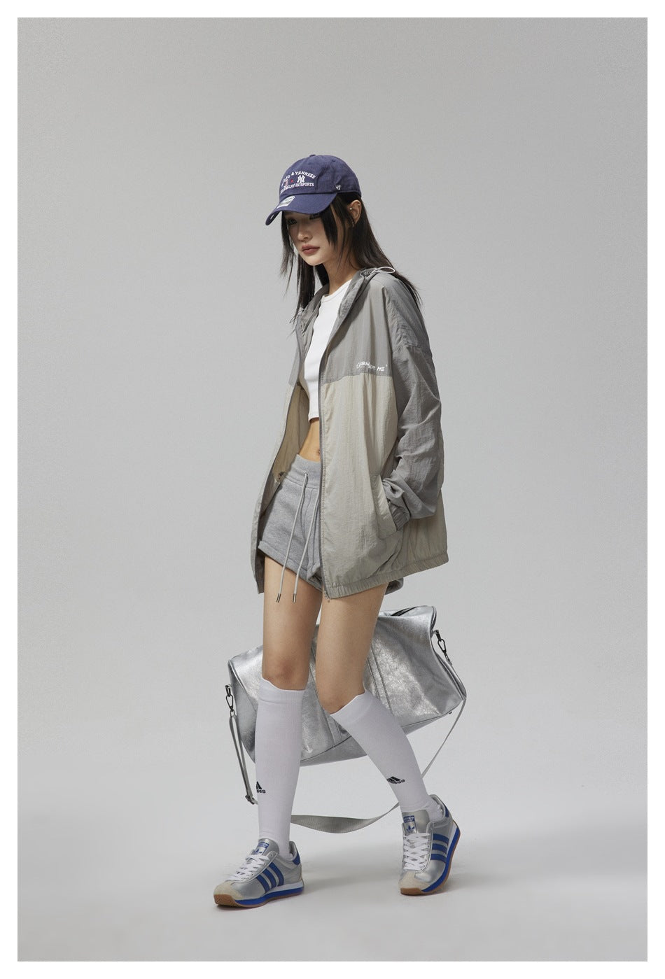 Model wearing an open gray and cream color-block hooded jacket, shown from a three-quarter angle.