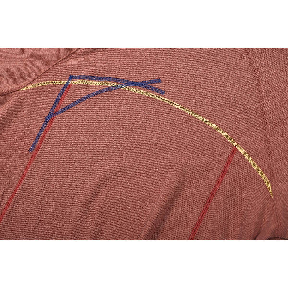 Close-up of dusty rose ribbed fabric with contrasting blue, yellow, and red stitching.