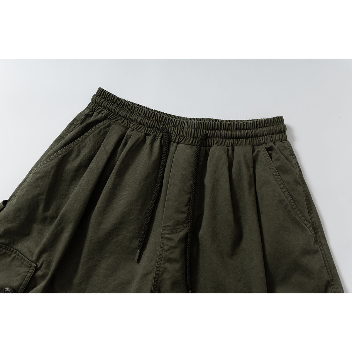 Close-up of olive wide-leg cargo shorts showing the elastic drawstring waist and angled front pockets.