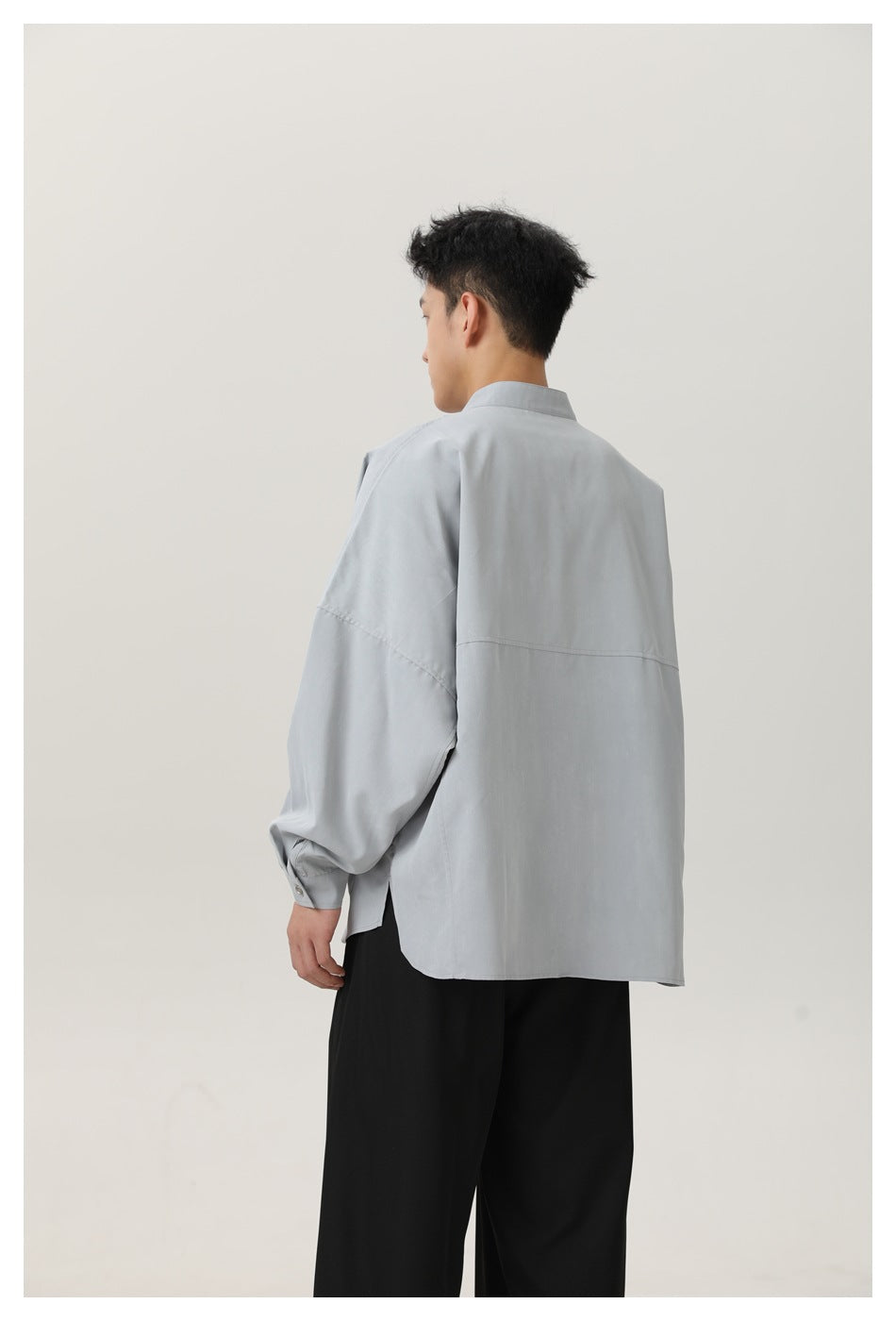 Back view of a model in a light gray oversized shirt with a back yoke seam and black pants