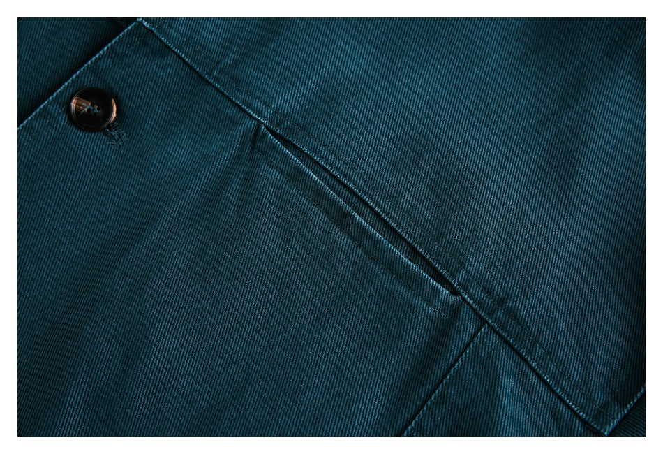 Close-up of a dark button and stitched flap on teal twill fabric.