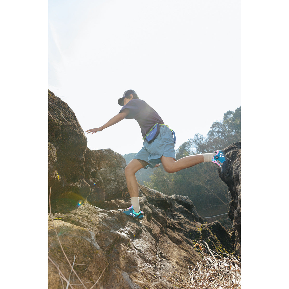 Hiker in a dark T-shirt and light blue shorts leaping across rocks outdoors.