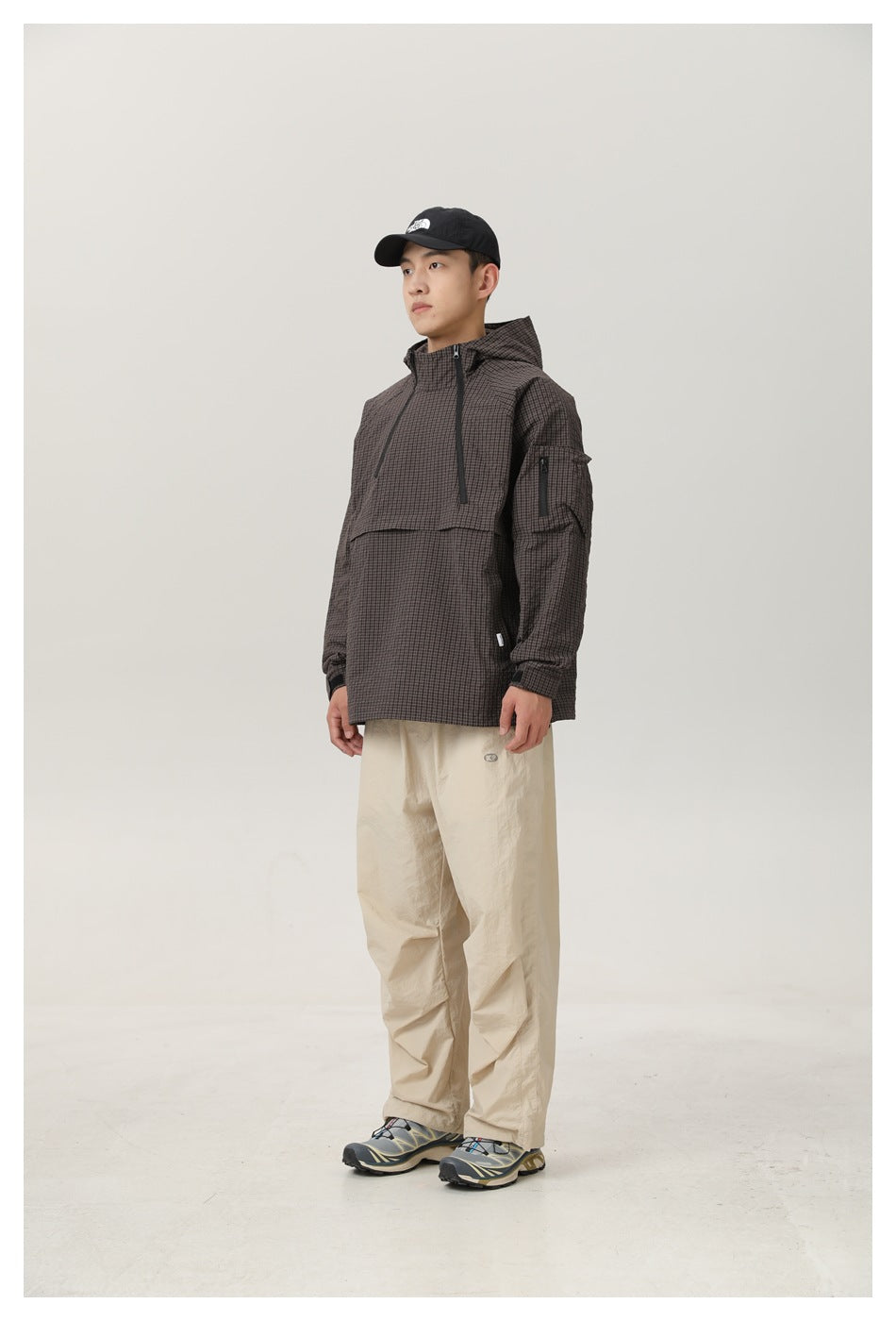 Model wearing dark checked hooded half-zip jacket with beige pants, shown from a three-quarter front angle