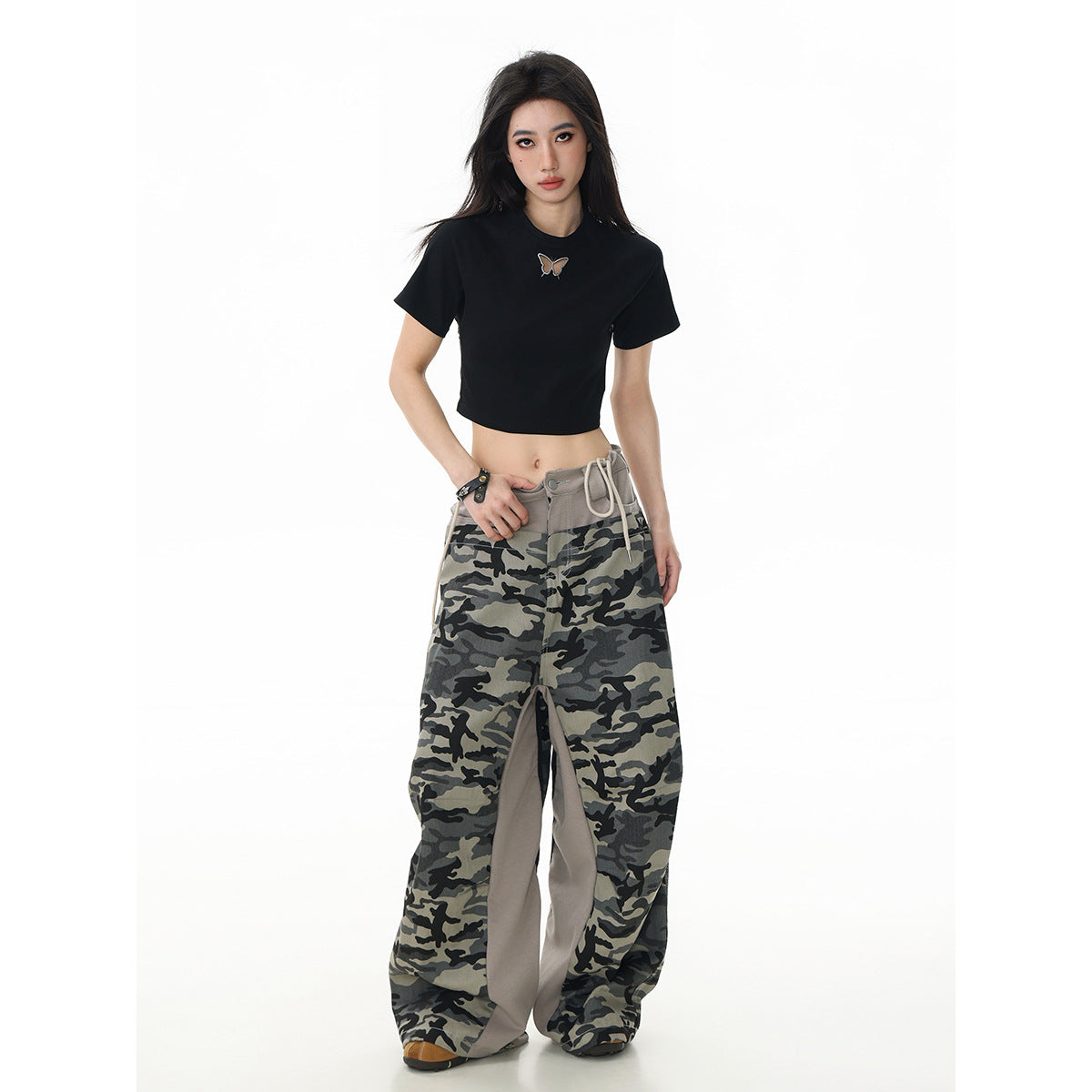 Full-length front view of a model in a black butterfly T-shirt and very loose gray camouflage pants.