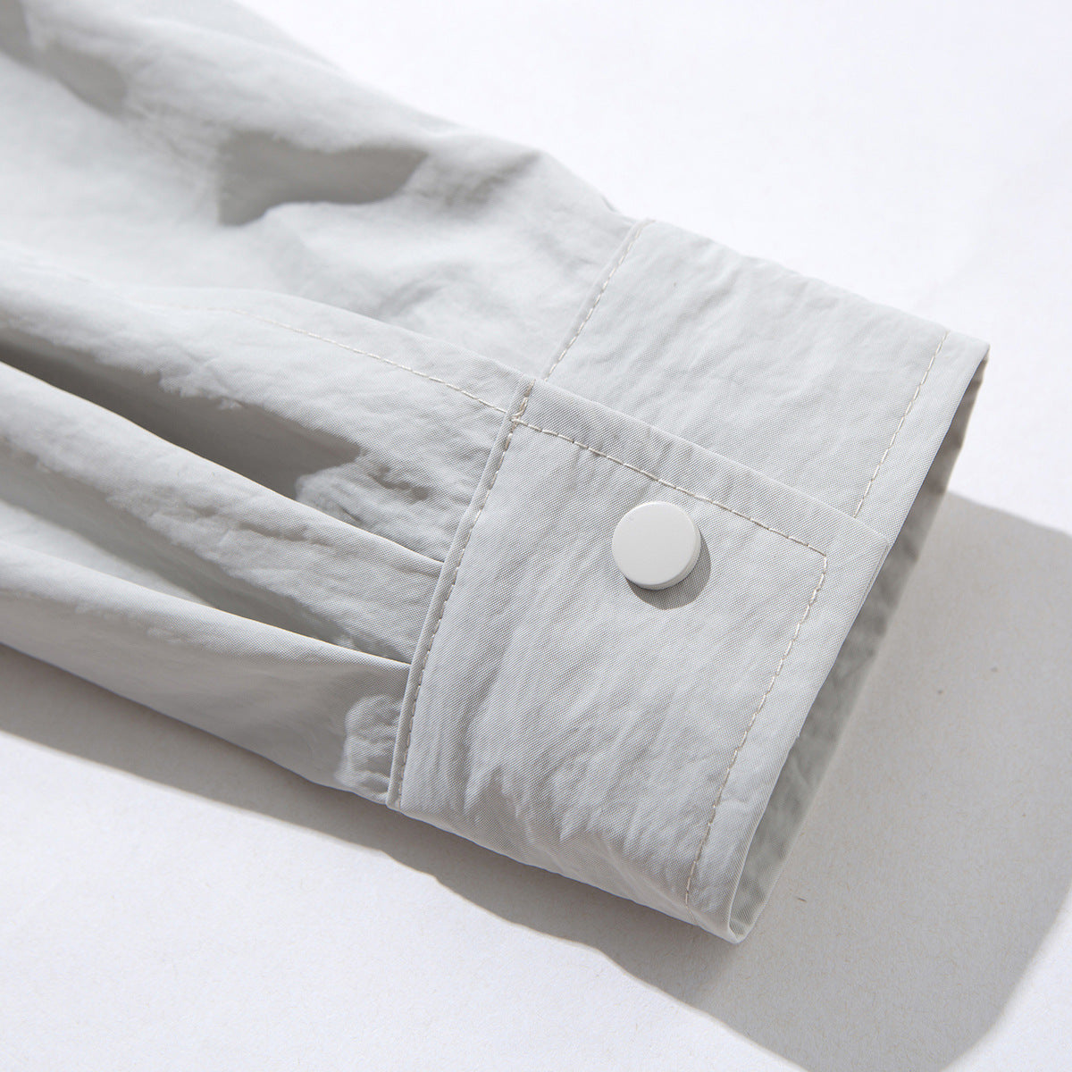Close-up of a pale gray jacket sleeve cuff with a white snap button and stitched seams.