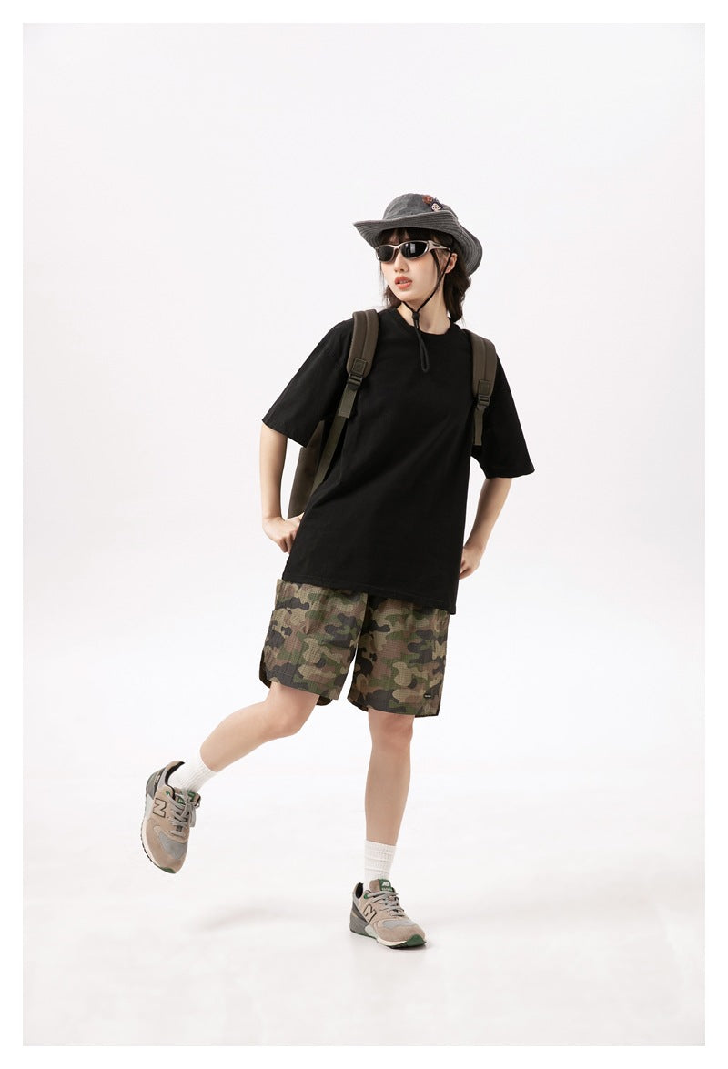 Model wearing camouflage shorts with a black T-shirt, bucket hat, sunglasses, backpack and sneakers