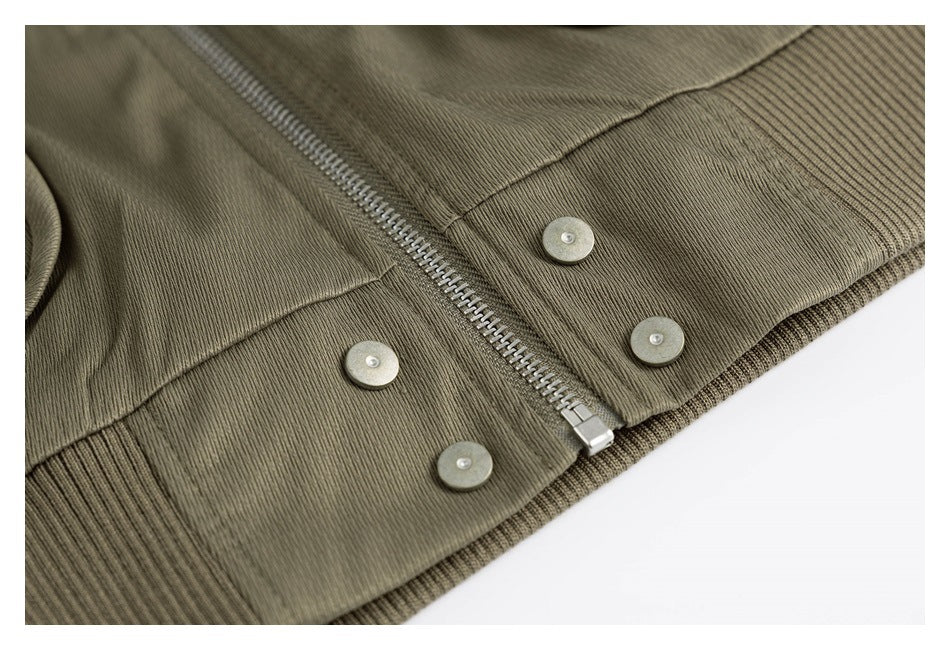 Close-up of an olive garment's metal zipper, snap buttons, and ribbed hem.