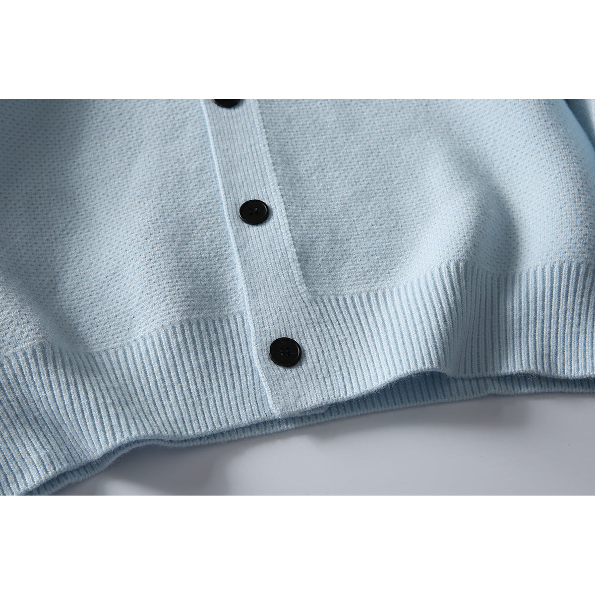Close-up of a pale blue cardigan's textured knit, black buttons and ribbed hem.