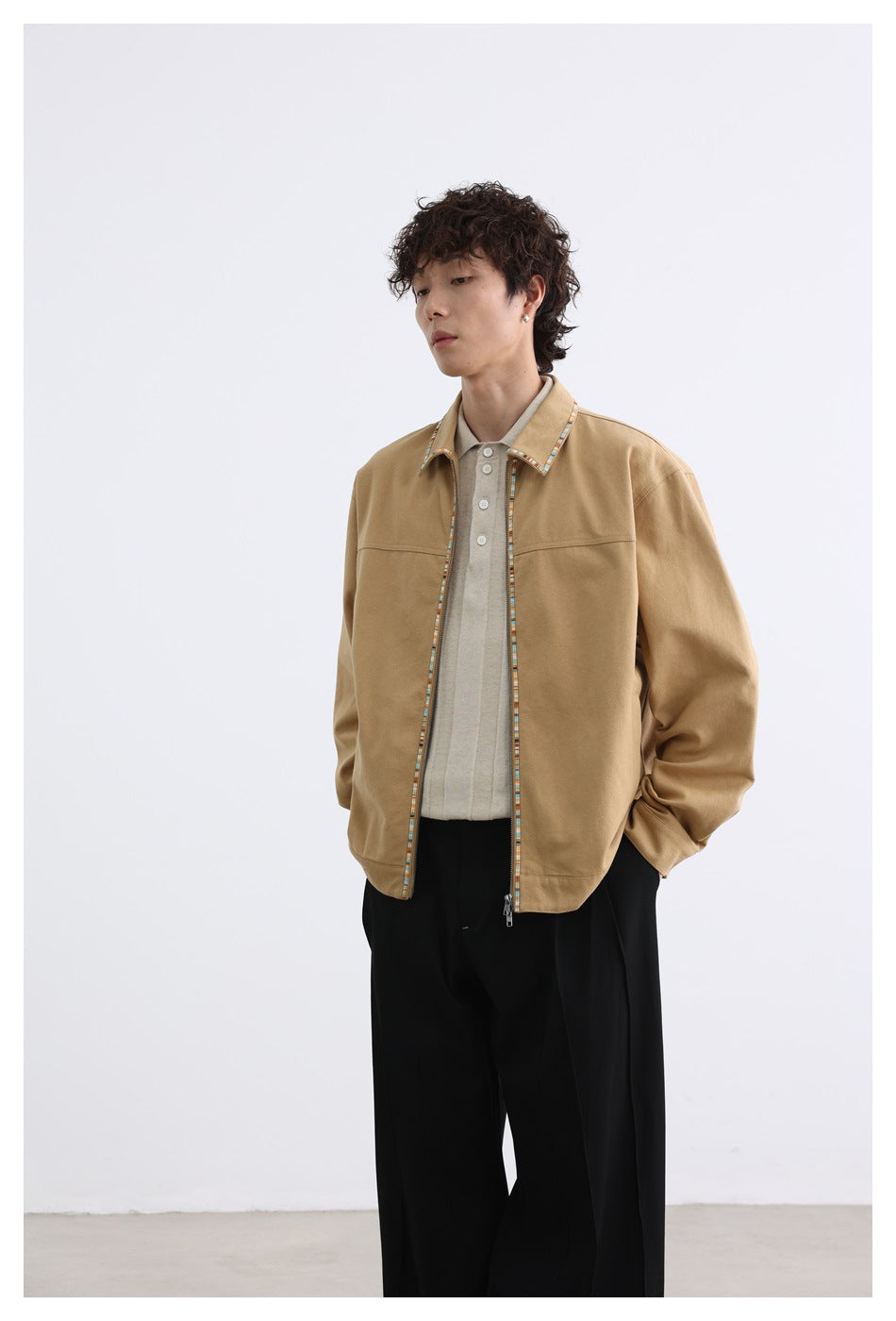 Model wearing a tan zip-front jacket with multicolor trim over a light polo and black wide-leg trousers, front view.