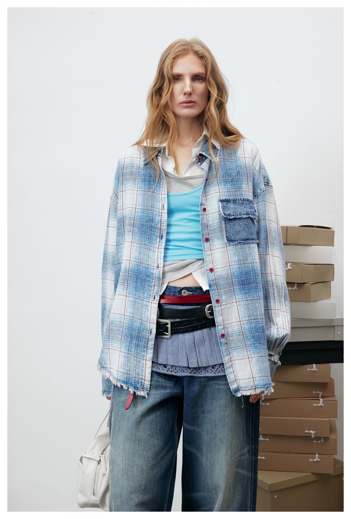 Close-up of a model wearing the open blue plaid shirt with denim pocket over a blue tank top, belts and jeans