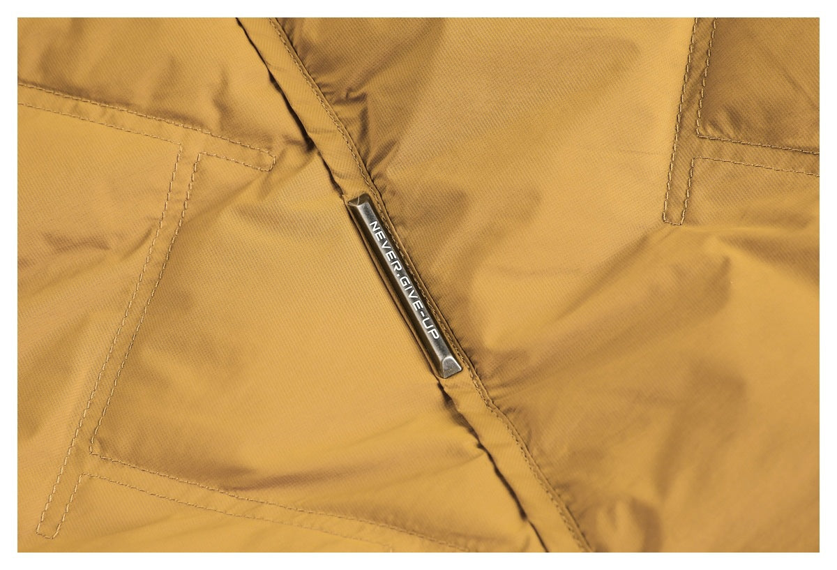 Close-up of mustard-yellow jacket stitching and a metal trim piece engraved “NEVER GIVE UP.”